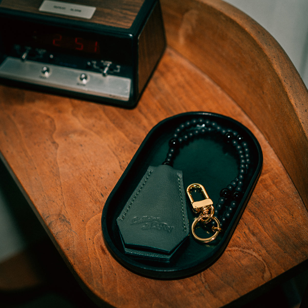 Key Coffin in green leather on a black tray next to a clock, lifestyle shot