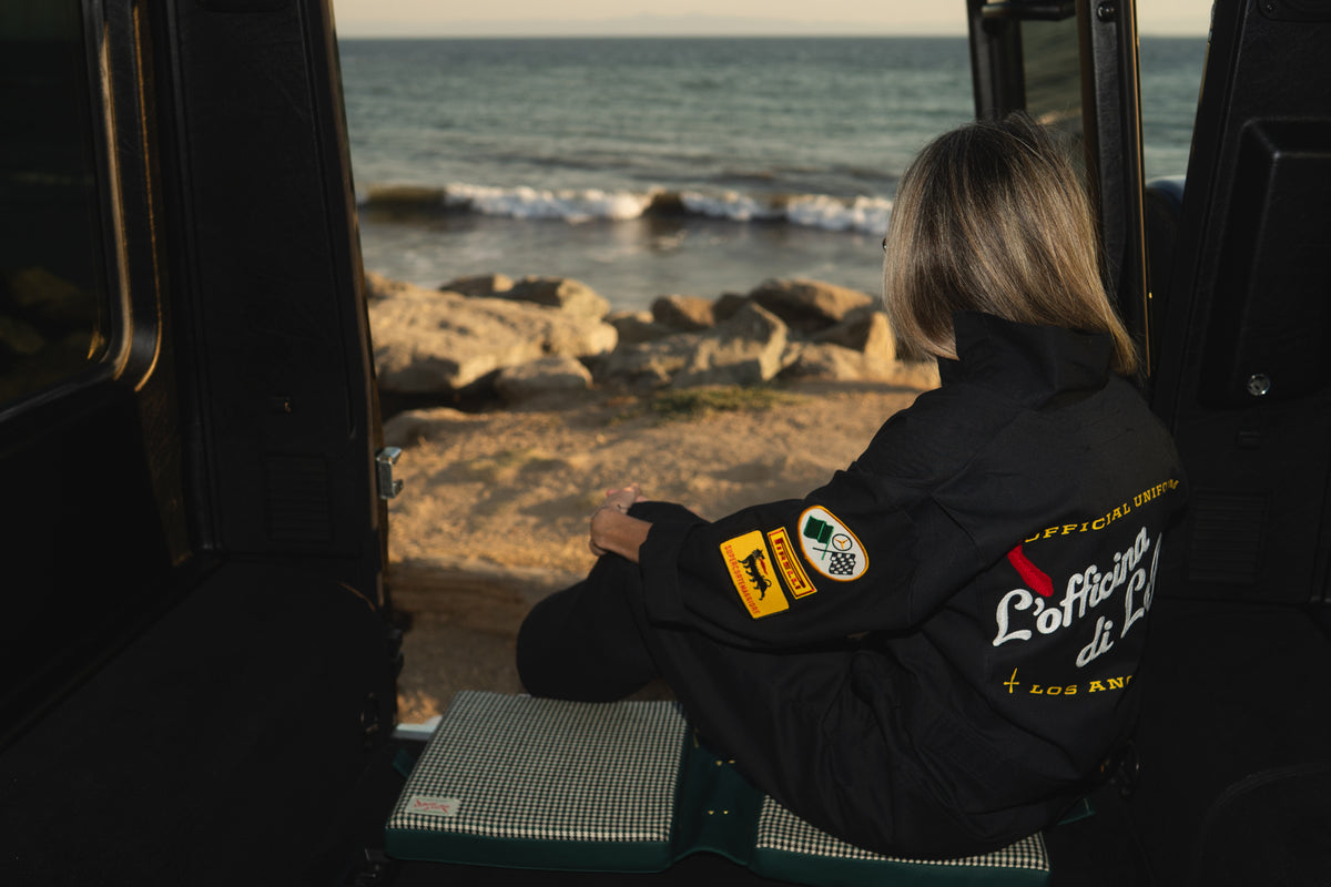 Person sitting inside a vehicle looking out at a rocky coastline with ocean waves.