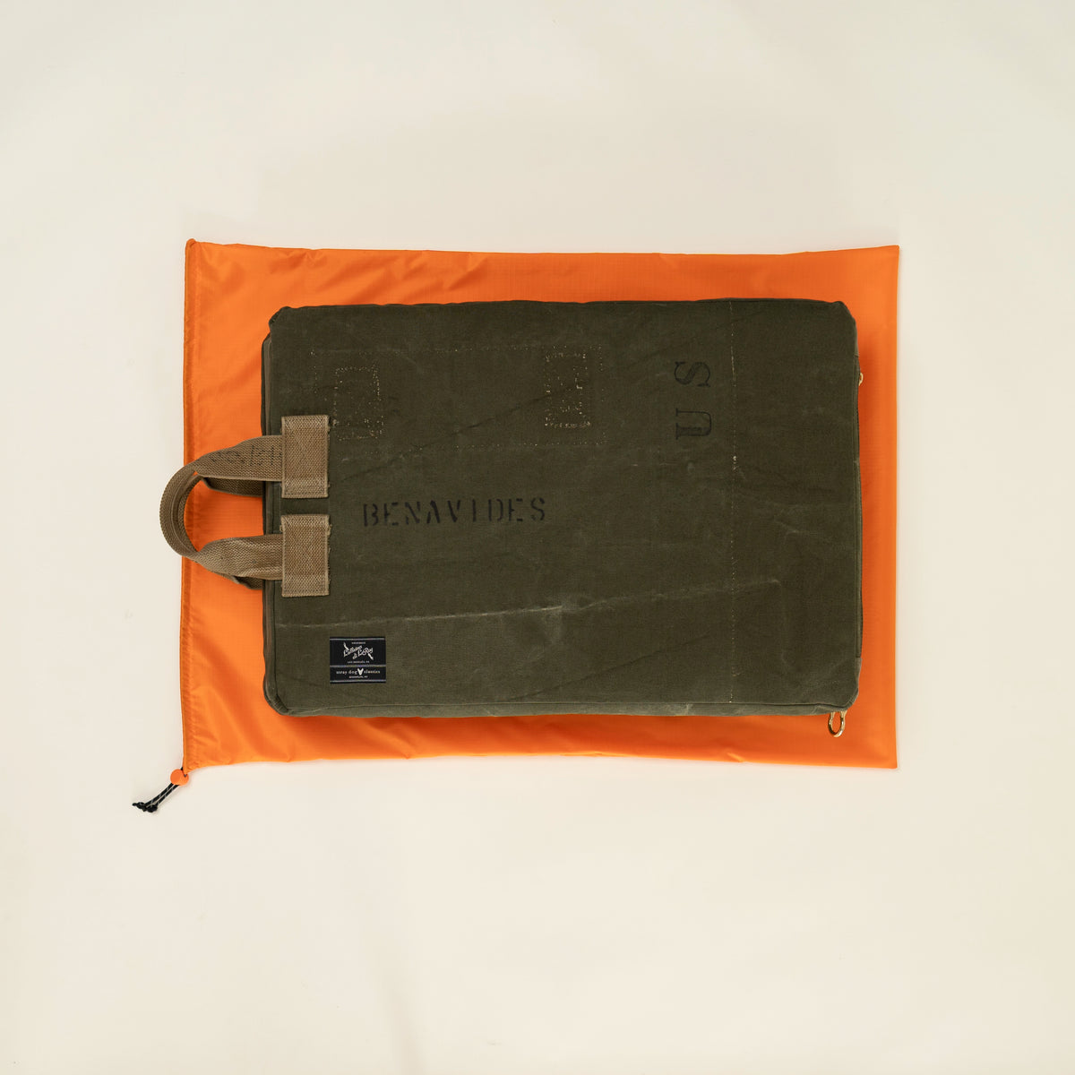 Tailgate cushion made from a reclaimed U.S. military canvas duffel stenciled "Benavides," shown on an orange drawstring bag