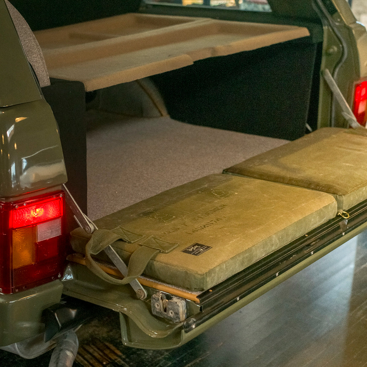 Two canvas tailgate cushions laid across the open tailgate of a green Range Rover Classic