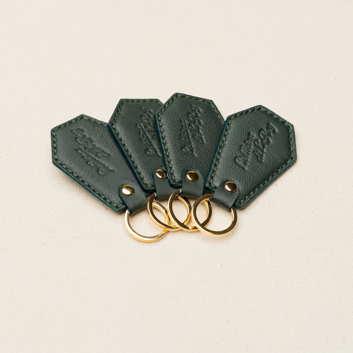 Four Coffin Key Fobs in forest green leather with brass rings on a beige background